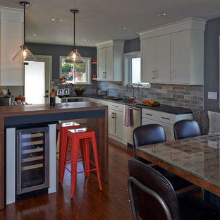 Mid-sized midcentury galley eat-in kitchen in Seattle with shaker cabinets, white cabinets, soapstone benchtops, green splashback, stainless steel appliances, medium hardwood floors, a farmhouse sink, slate splashback, with island and brown floor.