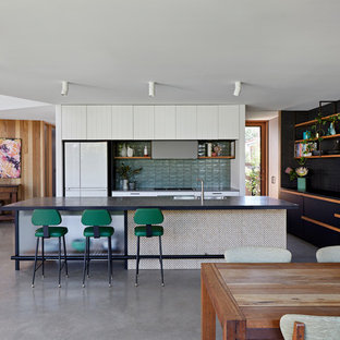 Scandinavian single-wall open plan kitchen in Melbourne with a drop-in sink, flat-panel cabinets, white cabinets, green splashback, white appliances, concrete floors, with island, grey floor and black benchtop.