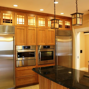Photo of a large arts and crafts l-shaped eat-in kitchen in DC Metro with a farmhouse sink, shaker cabinets, light wood cabinets, granite benchtops, green splashback, ceramic splashback, stainless steel appliances, ceramic floors, with island and black benchtop.