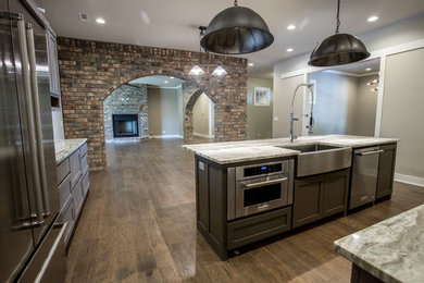 Inspiration for a large transitional l-shaped dark wood floor kitchen remodel in Other with a farmhouse sink, shaker cabinets, dark wood cabinets, granite countertops, gray backsplash, stone tile backsplash, stainless steel appliances and an island