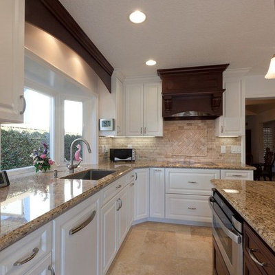 Example of a mid-sized transitional l-shaped travertine floor eat-in kitchen design in Orange County with a drop-in sink, raised-panel cabinets, white cabinets, granite countertops, beige backsplash, subway tile backsplash, stainless steel appliances and an island