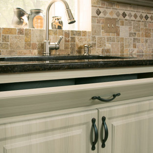 Photo of a large beach style u-shaped eat-in kitchen in New York with a single-bowl sink, raised-panel cabinets, distressed cabinets, granite benchtops, beige splashback, ceramic splashback, white appliances, ceramic floors, beige floor and black benchtop.