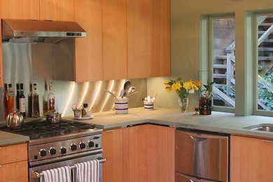 Ejemplo de cocinas en L actual de tamaño medio con armarios con paneles lisos, puertas de armario de madera oscura, encimera de acrílico y electrodomésticos de acero inoxidable
