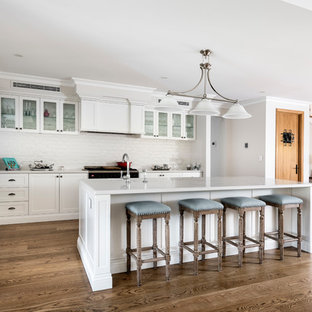 This is an example of a large traditional l-shaped kitchen in Perth with recessed-panel cabinets, white cabinets, quartz benchtops, white splashback, subway tile splashback, with island, white benchtop, medium hardwood floors, brown floor, an undermount sink and panelled appliances.