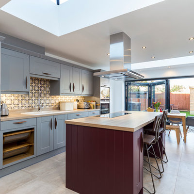 Example of a large transitional single-wall ceramic tile eat-in kitchen design in London with a double-bowl sink, shaker cabinets, blue cabinets, wood countertops, multicolored backsplash, an island, ceramic backsplash and stainless steel appliances