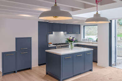 This is an example of a medium sized contemporary l-shaped kitchen/diner in London with a built-in sink, beaded cabinets, grey cabinets, composite countertops, stainless steel appliances, light hardwood flooring, an island and beige floors.