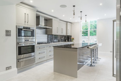 Inspiration for a medium sized contemporary single-wall kitchen in Hertfordshire with a submerged sink, flat-panel cabinets, grey cabinets, granite worktops, metallic splashback, metal splashback, an island and white floors.