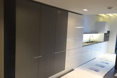 Photo of an expansive modern l-shaped kitchen/diner in London with an integrated sink, flat-panel cabinets, white cabinets, quartz worktops, white splashback, cement tile splashback, stainless steel appliances, ceramic flooring and an island.