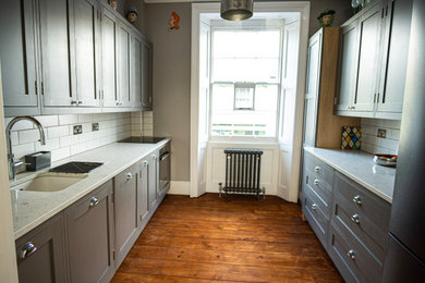 Imagen de cocina cerrada con armarios estilo shaker, puertas de armario grises, salpicadero blanco, salpicadero de azulejos de porcelana, electrodomésticos negros y encimeras blancas