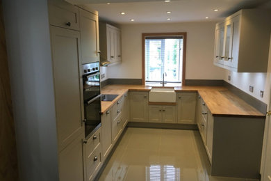 This is an example of a medium sized u-shaped enclosed kitchen with a submerged sink, recessed-panel cabinets, grey cabinets, wood worktops, grey splashback, ceramic flooring and green floors.