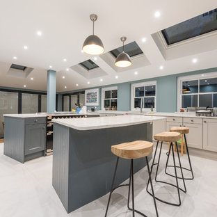 This is an example of a large classic l-shaped kitchen in Surrey with a submerged sink, recessed-panel cabinets, multiple islands, beige cabinets, green splashback, black appliances, beige floors and beige worktops.