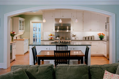 Example of a mid-sized classic l-shaped light wood floor eat-in kitchen design in DC Metro with an undermount sink, flat-panel cabinets, white cabinets, granite countertops, white backsplash, ceramic backsplash, stainless steel appliances and an island