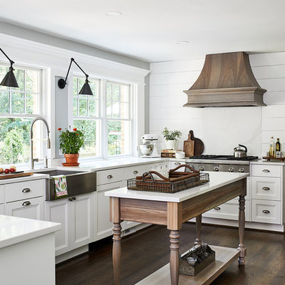 Example of a mid-sized country u-shaped dark wood floor and brown floor eat-in kitchen design in DC Metro with white backsplash, stainless steel appliances, an island, white countertops, a farmhouse sink, recessed-panel cabinets and white cabinets