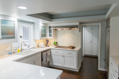 Inredning av ett klassiskt mellanstort kök och matrum, med en undermonterad diskho, luckor med infälld panel, vita skåp, bänkskiva i kvarts, grönt stänkskydd, stänkskydd i glaskakel, rostfria vitvaror, mörkt trägolv och en halv köksö