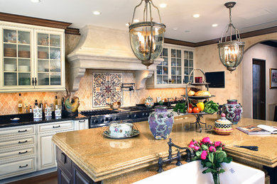 Large tuscan u-shaped dark wood floor eat-in kitchen photo in Los Angeles with white cabinets, an island, a farmhouse sink, glass-front cabinets, granite countertops, multicolored backsplash, stainless steel appliances and stone tile backsplash