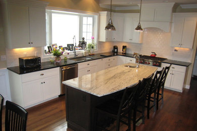 Inspiration for a mid-sized l-shaped medium tone wood floor open concept kitchen remodel in Boston with an undermount sink, raised-panel cabinets, white cabinets, granite countertops, white backsplash, porcelain backsplash, stainless steel appliances and an island