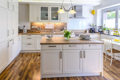 Inspiration for a medium sized traditional l-shaped open plan kitchen in Oxfordshire with a single-bowl sink, shaker cabinets, white cabinets, wood worktops, white splashback, glass sheet splashback, stainless steel appliances, medium hardwood flooring and an island.