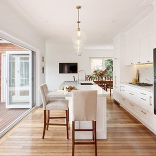 Inspiration for a mid-sized transitional single-wall kitchen in Sydney with shaker cabinets, white cabinets, granite benchtops, grey splashback, black appliances, medium hardwood floors, with island, a single-bowl sink and grey benchtop.