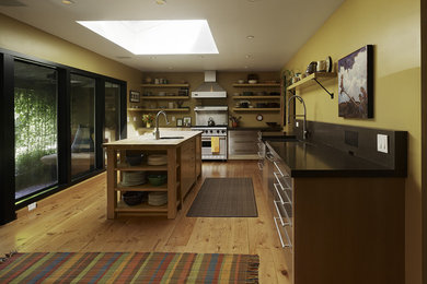 Example of a mid-sized trendy l-shaped light wood floor enclosed kitchen design in San Francisco with stainless steel appliances, stainless steel cabinets, open cabinets, a farmhouse sink, an island and solid surface countertops