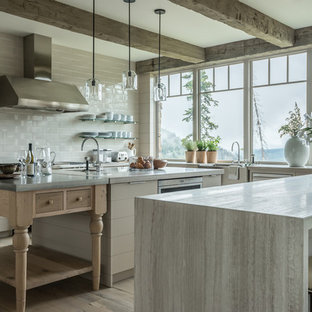 Ejemplo de cocina en U, rural, con fregadero sobremueble, armarios con paneles lisos, puertas de armario beige, salpicadero blanco, electrodomésticos de acero inoxidable, suelo de madera clara, una isla, suelo beige y encimeras grises