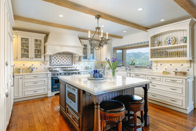 Inspiration for a large mediterranean u-shaped medium tone wood floor eat-in kitchen remodel in Santa Barbara with a farmhouse sink, white cabinets, ceramic backsplash, white backsplash, an island, recessed-panel cabinets, quartzite countertops and colored appliances