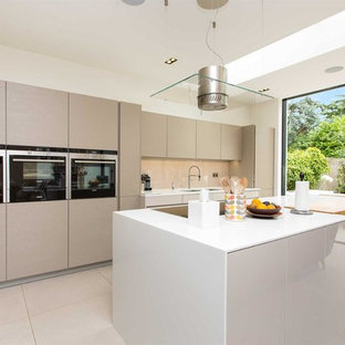 This is an example of a medium sized contemporary galley kitchen/diner in London with a double-bowl sink, flat-panel cabinets, beige cabinets, quartz worktops, glass sheet splashback, stainless steel appliances, an island, beige floors, white worktops and beige splashback.