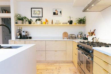 Photo of a medium sized contemporary l-shaped kitchen/diner in London with a double-bowl sink, flat-panel cabinets, light wood cabinets, integrated appliances and an island.