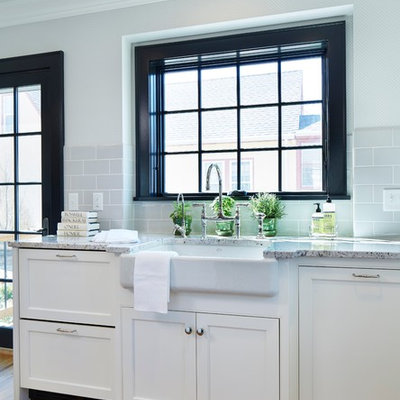 Transitional u-shaped medium tone wood floor kitchen photo in Minneapolis with a farmhouse sink, shaker cabinets, white cabinets, granite countertops, gray backsplash, subway tile backsplash, paneled appliances and an island