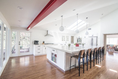 Inspiration for a mid-sized transitional l-shaped medium tone wood floor and brown floor open concept kitchen remodel in Los Angeles with recessed-panel cabinets, white cabinets, quartz countertops, white backsplash, wood backsplash, stainless steel appliances, an island and white countertops
