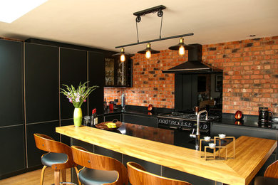 This is an example of a large contemporary open plan kitchen in Other with an integrated sink, flat-panel cabinets, black cabinets, quartz worktops, black splashback, glass sheet splashback, black appliances, bamboo flooring, an island and black worktops.
