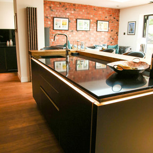 Inspiration for a large contemporary open plan kitchen in Other with an integrated sink, flat-panel cabinets, black cabinets, quartzite benchtops, black splashback, glass sheet splashback, black appliances, bamboo floors, with island and black benchtop.