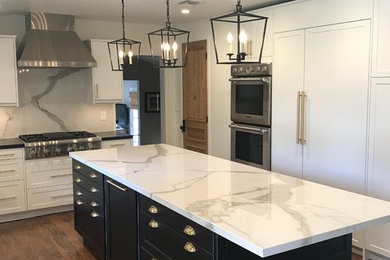 Inspiration for a mid-sized transitional medium tone wood floor and brown floor kitchen remodel in Other with a farmhouse sink, shaker cabinets, white cabinets, granite countertops, white backsplash, porcelain backsplash, paneled appliances and an island