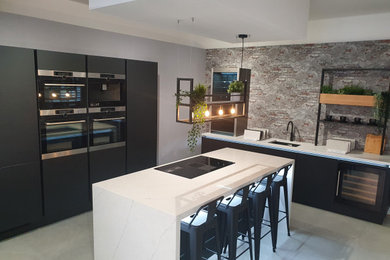 Medium sized contemporary l-shaped open plan kitchen in Cheshire with a built-in sink, flat-panel cabinets, black cabinets, quartz worktops, multi-coloured splashback, integrated appliances, porcelain flooring, an island, grey floors and white worktops.
