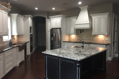 Enclosed kitchen - large transitional u-shaped dark wood floor and brown floor enclosed kitchen idea in Dallas with an undermount sink, raised-panel cabinets, white cabinets, granite countertops, beige backsplash, stone tile backsplash, stainless steel appliances and an island