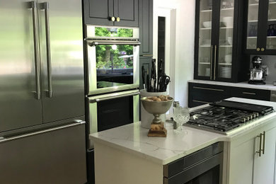 Mid-sized transitional u-shaped light wood floor and white floor eat-in kitchen photo in Cleveland with an undermount sink, shaker cabinets, black cabinets, white backsplash, marble backsplash, stainless steel appliances, an island, white countertops and quartz countertops