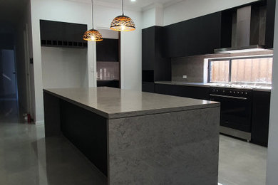 Huge minimalist galley cement tile floor open concept kitchen photo in Sydney with an undermount sink, flat-panel cabinets, black cabinets, quartz countertops, gray backsplash, quartz backsplash, black appliances, two islands and gray countertops