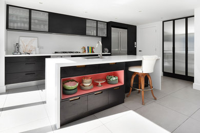 Example of a trendy galley enclosed kitchen design in London with an undermount sink, glass-front cabinets, white backsplash, stainless steel appliances and an island