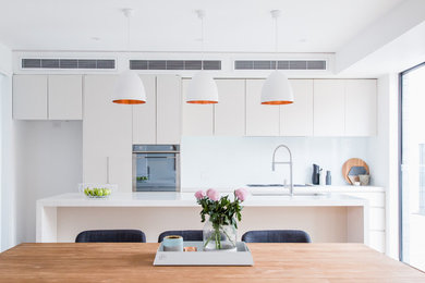 Inspiration for a medium sized contemporary open plan kitchen in Melbourne with a built-in sink, flat-panel cabinets, white cabinets, wood worktops, white splashback, ceramic splashback, white appliances, light hardwood flooring, an island and white worktops.