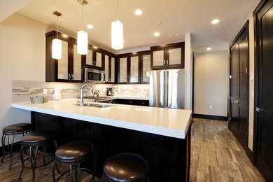 Example of a mid-sized classic u-shaped medium tone wood floor and brown floor enclosed kitchen design in Salt Lake City with an undermount sink, glass-front cabinets, dark wood cabinets, quartz countertops, beige backsplash, cement tile backsplash, stainless steel appliances and an island