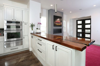 Modern inredning av ett mellanstort brun brunt kök, med skåp i shakerstil, vita skåp, träbänkskiva, rostfria vitvaror, mörkt trägolv, en halv köksö och brunt golv