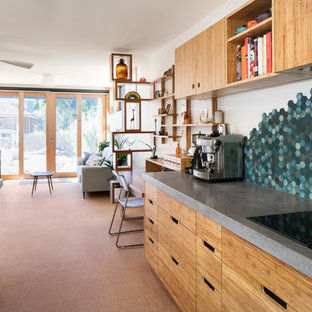 Diseño de cocina en U, actual, de tamaño medio, abierta, con fregadero bajoencimera, armarios con paneles lisos, puertas de armario de madera clara, encimera de cemento, salpicadero gris, salpicadero de azulejos de piedra, suelo de corcho, una isla y suelo beige