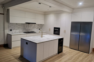 Modern inredning av ett mellanstort grå grått kök, med en undermonterad diskho, luckor med upphöjd panel, vita skåp, bänkskiva i kvarts, grått stänkskydd, stänkskydd i sten, svarta vitvaror, mellanmörkt trägolv, en köksö och beiget golv