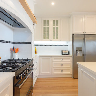 Open concept kitchen - large traditional l-shaped light wood floor open concept kitchen idea in Melbourne with an undermount sink, recessed-panel cabinets, white cabinets, quartz countertops, white backsplash, subway tile backsplash, black appliances and an island
