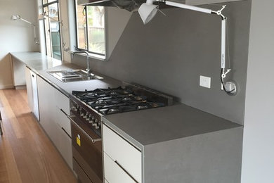 Photo of a modern kitchen in Melbourne with a built-in sink, flat-panel cabinets, white cabinets, engineered stone countertops, grey splashback, stainless steel appliances, medium hardwood flooring and an island.