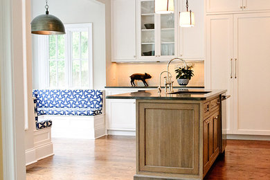 Klassisk inredning av ett stort kök och matrum, med en undermonterad diskho, skåp i shakerstil, vita skåp, grått stänkskydd, stänkskydd i tunnelbanekakel, integrerade vitvaror, mellanmörkt trägolv och en köksö