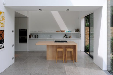 Large contemporary galley kitchen/diner in London with an integrated sink, engineered stone countertops, white splashback, glass sheet splashback, limestone flooring and an island.