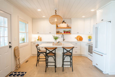 Example of a mid-sized beach style l-shaped light wood floor and beige floor eat-in kitchen design in Other with an undermount sink, shaker cabinets, white cabinets, quartz countertops, white backsplash, subway tile backsplash, white appliances, an island and white countertops