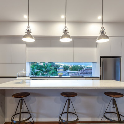 Mid-sized trendy single-wall medium tone wood floor open concept kitchen photo in Brisbane with white cabinets, marble countertops, stainless steel appliances, an island, flat-panel cabinets, an undermount sink and window backsplash