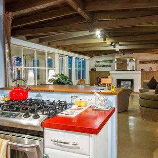 Design ideas for a mid-sized midcentury l-shaped kitchen in Phoenix with a farmhouse sink, flat-panel cabinets, white cabinets, recycled glass benchtops, stainless steel appliances, concrete floors and no island.