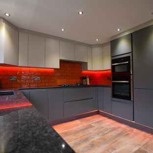 Design ideas for a medium sized contemporary u-shaped kitchen in Other with a submerged sink, flat-panel cabinets, grey cabinets, red splashback, metro tiled splashback, no island, brown floors and black worktops.